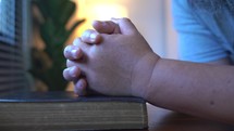 Close up hands praying on Bible at wooden table in morning, Christian concept.