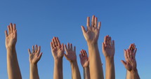 Male and female hands raised and held up on the background of clear blue sky. Solid vote or volunteers