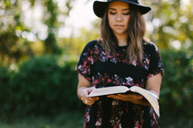 portrait of a young woman standing outdoors reading a Bible 