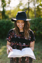 teen girl in a hat reading a Bible outdoors 