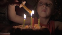 Slow motion view of small girl lighting the candles on birthday cake in the dark