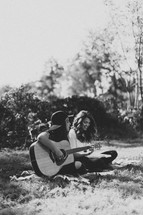 young women sitting on a blanket outdoors reading Bibles and playing a guitar
