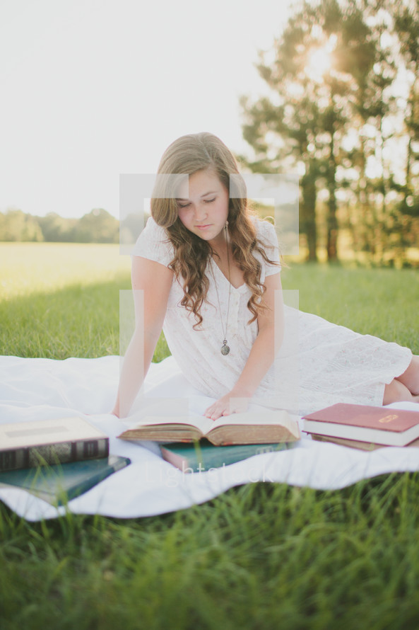 woman lying on a blanket in the grass reading books 