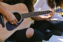 teen girls sitting on a blanket outdoors playing a guitar 