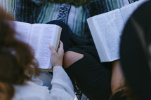 young woman sitting on a blanket outdoors reading Bibles 