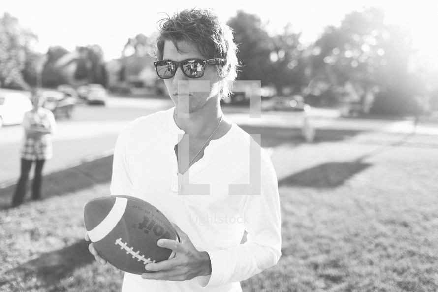 Man with sunglasses holding football in park