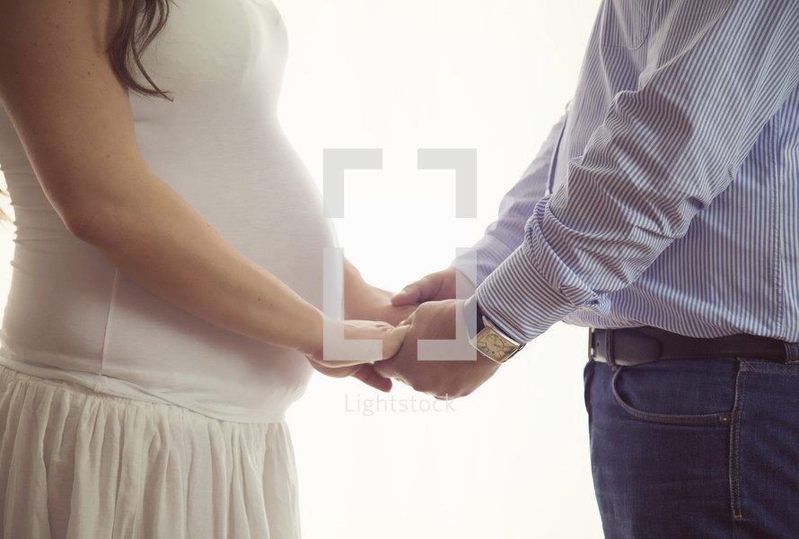 A man and pregnant woman facing each other and holding hands.
