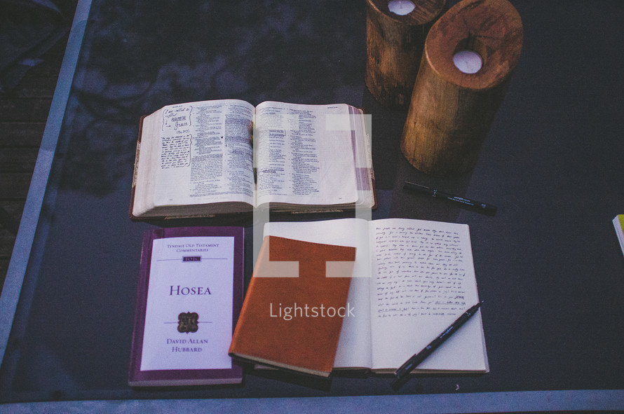 Open bible with the Book of Hosea and a journal on a glass table with candles.