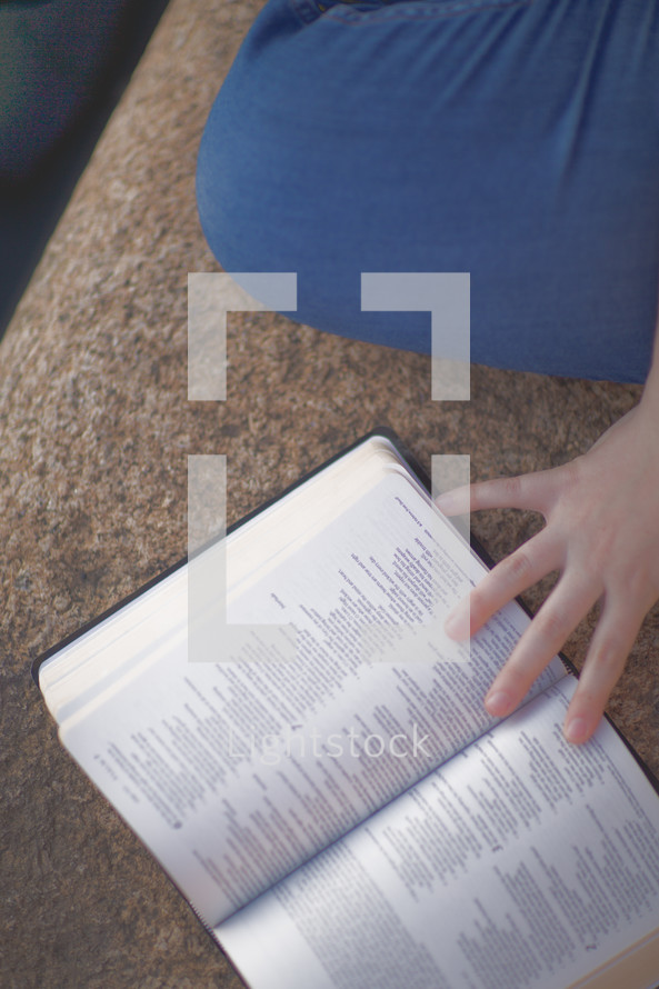 a woman sitting on concrete reading a Bible 