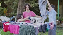 Three kids taking off laundry from the hanging line to the basket
