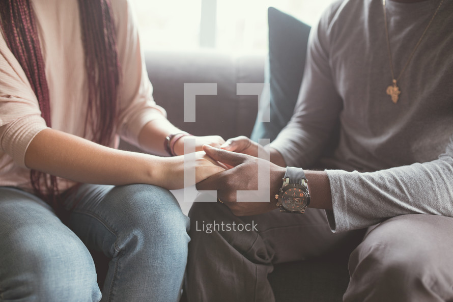 a couple holding hands sitting on a couch 