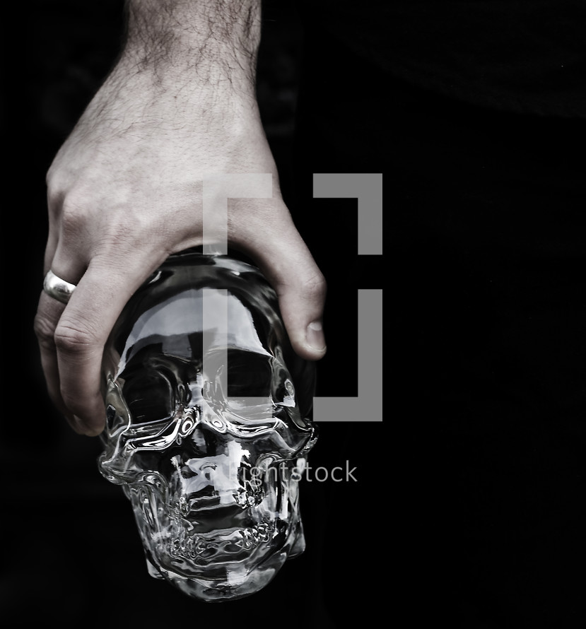 Man holding glass skull with ring on middle finger.