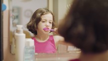 Little girl brushing her teeth in front of the mirror