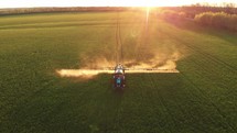 Aerial view of the tractor that irrigates the green field by special installation. Processing of a tractor in the field sprays the field at sunset. Chemical treatment of fields from pests, diseases.