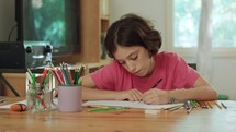 young girl sitting at the table drawing with colored pencils