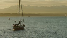 Sailboat heads out into open water with Olympic mountain range in background, slow-motion