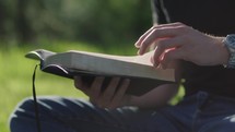 Young man reading his Bible outside on a warm sunny day