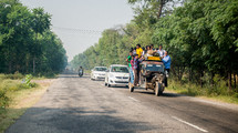 people loaded onto a crowded vehicle traveling on a road in India 