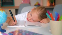 Portrait of exhausted sad primary child school girl studying feeling headache writing difficult assignment at home. Tired pupil schoolgirl writing hometask in notebook. The concept of online and home