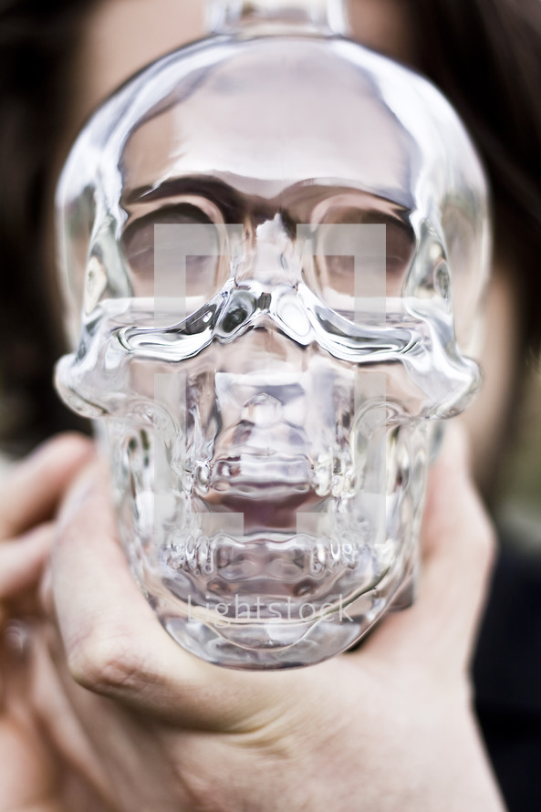 Man holding glass skull in front of face.