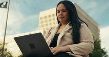 Young business woman walking around the city using her phone and laptop