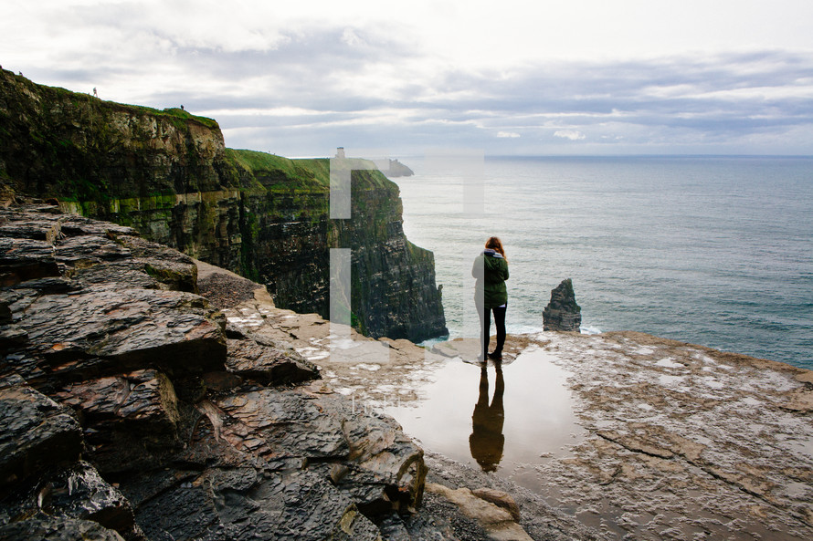 a woman standing at the edge of a sea cliff looking out over the ocean 