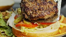 Large hamburger placed on a bun with vegetables in slow motion