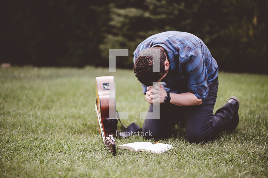 a man with a guitar praying outdoors reading a Bible 
