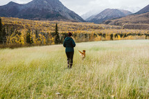 Woman and dog playing in field near mountains