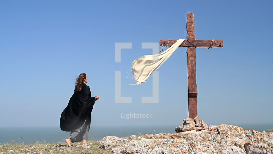 A woman in a black cape approaches the Holy Cross.
