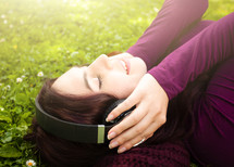 young woman listening to headphone in the grass