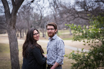 Expecting couple standing outside in a park with trees.