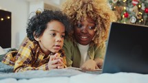 Mother and Kid Watching Cartoon on Laptop in Bedroom with Christmas Tree
