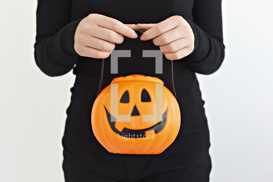 person holding a jack-o-lantern candy bucket 