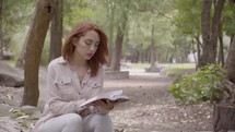 a woman reading a Bible in a park 