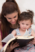 mother reading a Bible to her daughter 