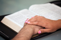 a couple holding hands over a Bible