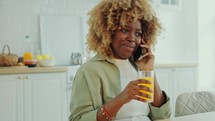 Young Woman Drinking Juice and Chatting on Phone at Home
