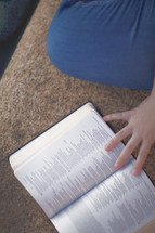 a woman sitting on concrete reading a Bible 