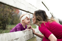 a mother kissing her toddler daughter through fence slats