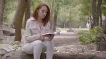 a woman walking in a park carrying a Bible and sitting down to read