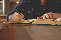 a woman sitting at a table reading a Bible and writing in a journal 