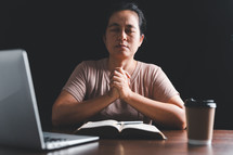 Asian woman praying with Bible and computer