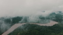 Drone aerial view of a murky river between dense Amazon Rainforest on a foggy day.