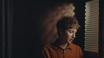 Young regretful woman speaking through perforated screen of confession booth when having private conversation with priest in church
