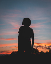 silhouette of a woman outdoors at sunset looking up 