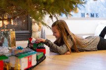 little girl playing with a toy train under a Christmas tree