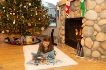 a girl reading a Christmas book in front of a fire place 