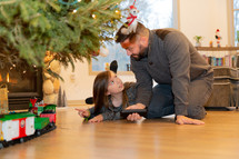 father and daughter playing with a toy train under a Christmas tree