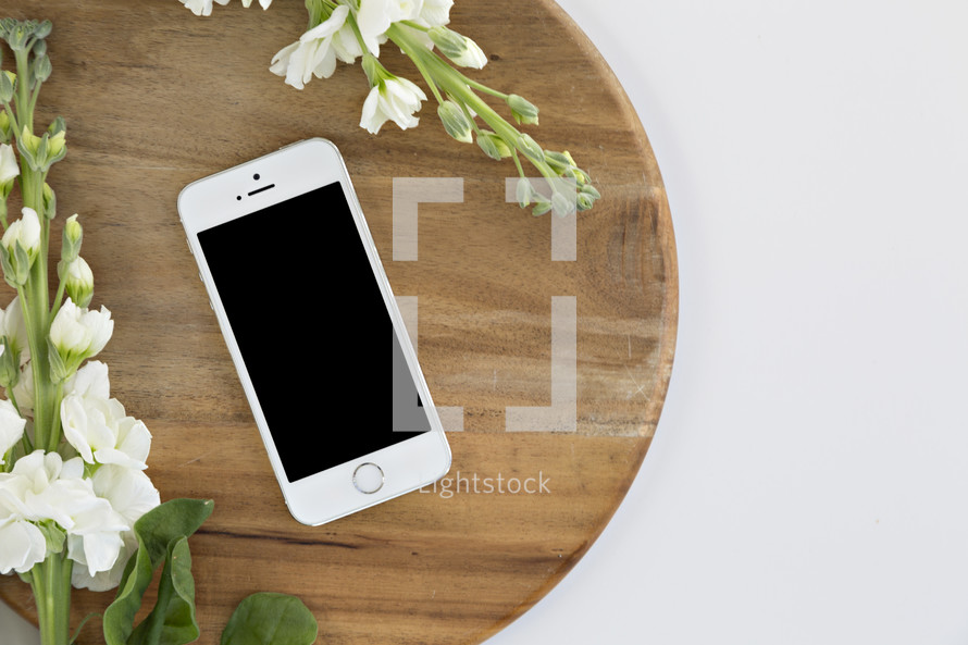 phone and white flowers on a cutting board against a white background 